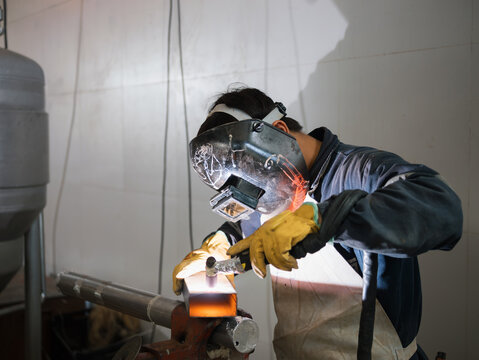 Welder in protective gear joining metal in workshop