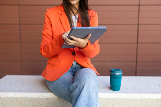 Woman in orange blazer working on a tablet outside