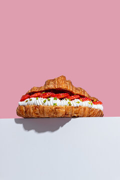 Croissant with strawberry and cream against pink backdrop