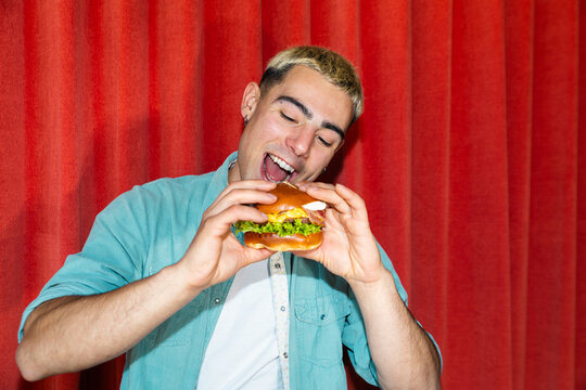 Man eating hamburger in front of red curtain backdrop