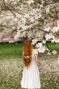 Woman in white dress under blooming magnolia branches