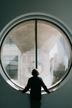 Person looking through round window at modern city scene