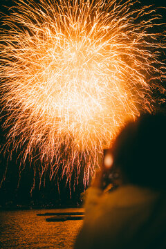 Golden fireworks burst lighting night sky over water