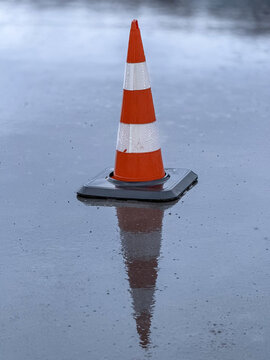 Orange traffic cone on wet road with reflection in rain