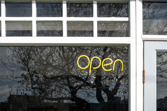 Open neon sign on shop window with tree reflection outside