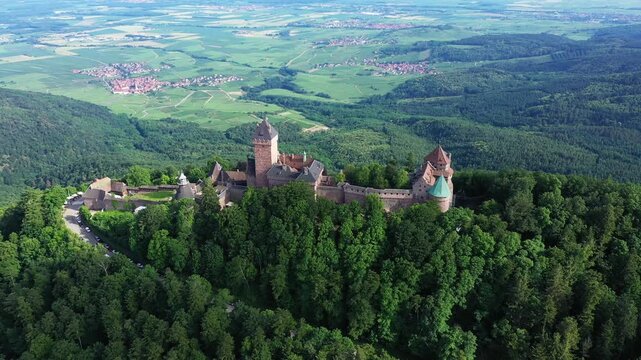 Drone shot of the historic Haut Koenigsbourg Castle surrounded by lush green forest and scenic countryside in Alsace, France.