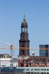 Obraz premium The historic St. Michaelis Church tower, known as Michel, with construction cranes in the foreground under a blue sky in Hamburg