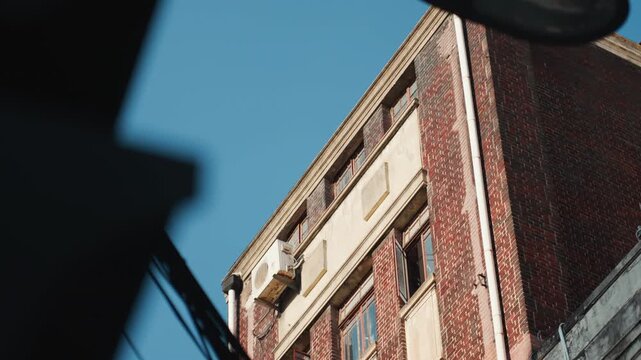Brick building corner under bright blue sky, closeup on weathered masonry and ornate cornice urban photographer captures texture and shadow while architect inspects structural detail, vintage fire