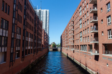 Naklejka premium A canal with dark blue water between large red brick warehouses and office buildings in Hamburg's Speicherstadt district