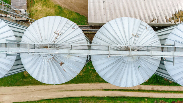 Aerial view of silver silos standing tall against the earth tones of the surrounding fields, contrasting textures and tones, Sremska Mitrovica, Vojvodina, Serbia.