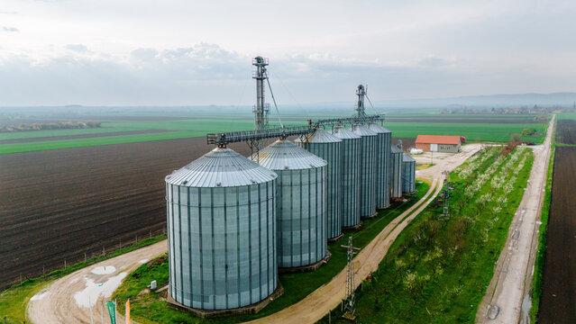 Aerial view of the silver silos standing tall against the backdrop of dark, tilled soil and vibrant green fields, Sremska Mitrovica, Vojvodina, Serbia.
