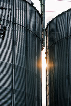 View of sunlight piercing through the gap between two towering metal silos, their corrugated surfaces reflecting the light in Sremska Mitrovica, Vojvodina, Serbia.