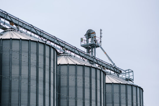 View of towering metallic grain silos gleaming under a muted sky, interconnected by conveyor structures, in Sremska Mitrovica, Vojvodina, Serbia.