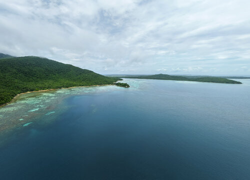 Aerial view of the deep blue sea meeting the lush green coastline under a cloudy sky at Annora beach, Karimunjawa, Jawa Tengah, Indonesia.