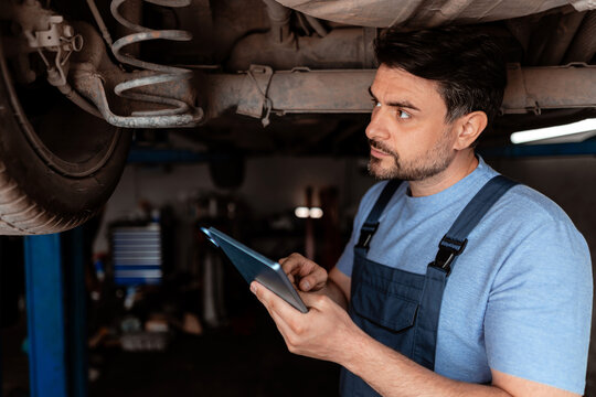 Car mechanic checks vehicle underbody with a tablet in a garage workshop in daytime