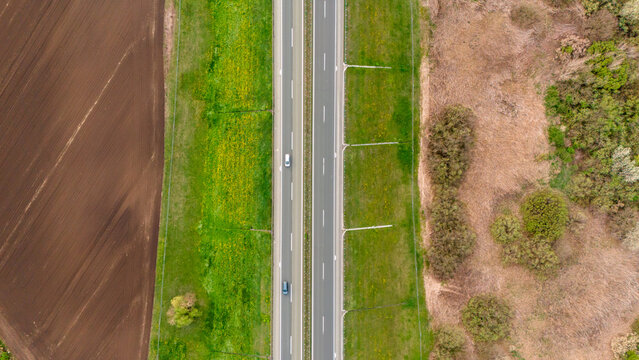 Aerial view of a straight highway cutting through a vivid landscape of freshly tilled brown fields, vibrant green meadows, and dry fields, Sremska Mitrovica, Vojvodina, Serbia.