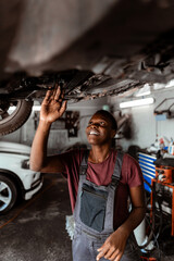 Obraz premium Worker repairs car under vehicle in garage during daytime in busy auto shop