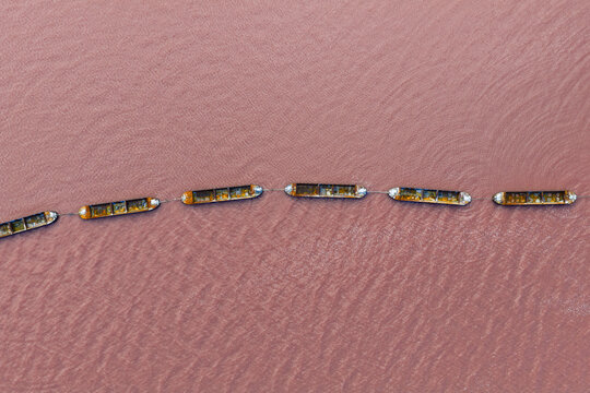 Aerial view of a chain of connected boats stand out against the vibrant pink hue of the water, creating a striking contrast, San Pedro del Pinatar, Region of Murcia, Spain.