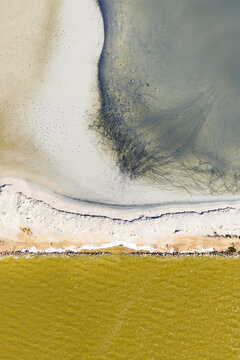 Aerial view of the vibrant yellow salt ponds meeting the serene beach and the tranquil sea, a mesmerizing blend of colors and textures, San Pedro del Pinatar, Region of Murcia, Spain.