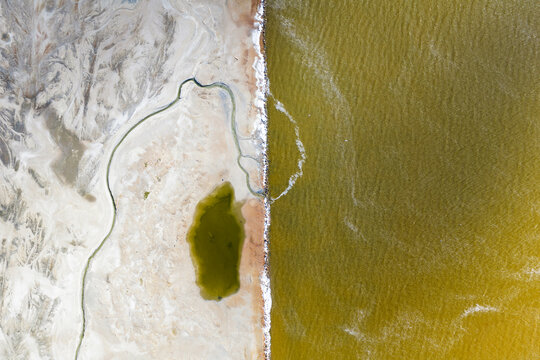 Aerial view of the stark contrast between the golden waters and the pale, textured earth, divided by a thin strip of shore, San Pedro del Pinatar, Region of Murcia, Spain.