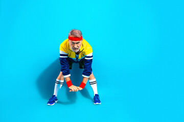 Naklejka premium Senior man stretching in retro sportswear on bright blue background showing fitness, active lifestyle and playful vintage workout attitude