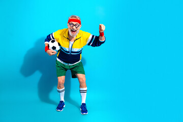 Obraz premium Cheerful senior man in retro sportswear holding a soccer ball and celebrating fitness and fun