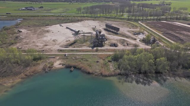 Aerial approaching view of abandoned sand quarry with rusting industrial machinery