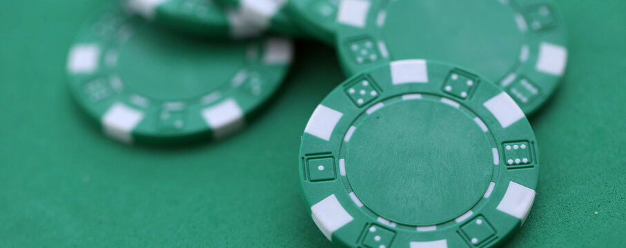 Green casino poker chips on green gaming table close up. Few amount of green casino chips
