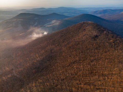 Aerial view of Ragac peak, with a wisp of smoke adding a touch of mystery to the serene landscape, Cerova vrchovina, Banska Bystrica Region, Slovakia.
