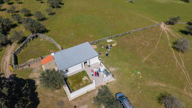 Aerial view of a white building with a grey roof nestled in a green field, surrounded by trees and stone walls, Evora, Portugal.