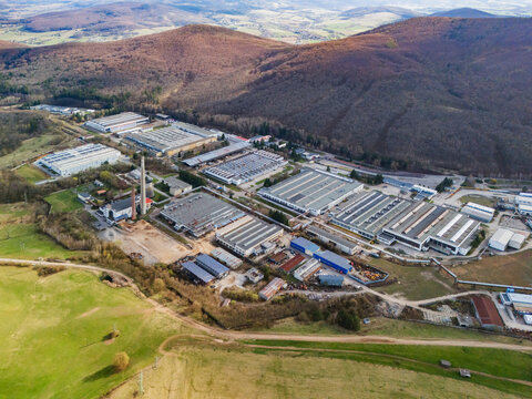 Aerial view of industrial buildings nestled amidst rolling hills and forests, a contrast of man-made structures and natural landscapes, Detva, Banskobystricky kraj, Slovakia.