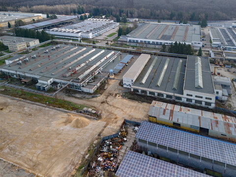 Aerial view of sprawling industrial buildings with varied roof textures and tones nestled near a dense forest, Detva, Banskobystricky kraj, Slovakia.