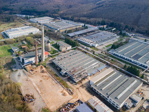 Aerial view of industrial buildings with red brick chimney stacks piercing the skyline, contrasting with the green trees, Detva, Banskobystricky kraj, Slovakia.
