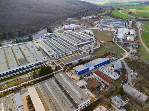 Aerial view of industrial buildings with grey roofs and blue accents nestled among vibrant green fields and dense forests, Detva, Banskobystricky kraj, Slovakia.