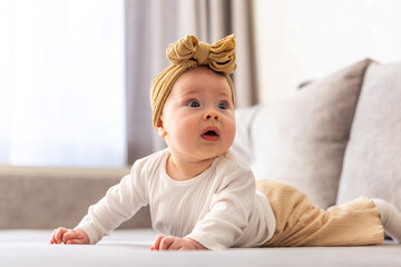 Fototapeta premium Adorable baby girl with a bow on her head exploring the world from a couch