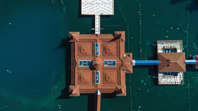 Aerial view of a distinctive building with a red-tiled roof surrounded by the tranquil, dark waters of Lake Heviz, Zala, Hungary.