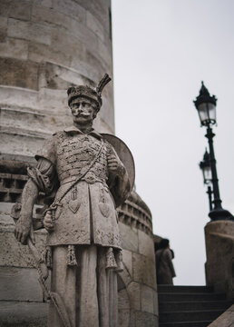 View of a stone soldier statue stands guard, its weathered face and ornate uniform a stark contrast to the smooth column behind, Budapest, Hungary.
