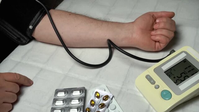 Individual measures blood pressure using a digital monitor while displaying medication and a relaxed arm on a soft surface in a home setting