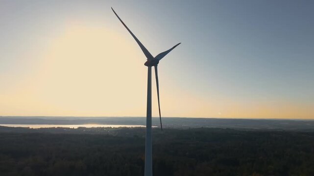 Wind turbine silhouette at sunset near Lake Starnberg in Bavaria, Germany. Scenic landscape with golden sky, water and countryside, representing renewable energy and sustainable future.