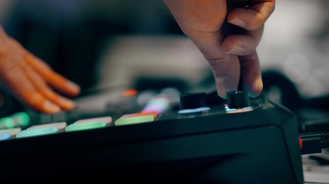 turning mixer knob audio controller colorful backlit pads music production. Producer adjusting sound levels digital audio workstation recording studio equipment. Electronic musician performing live