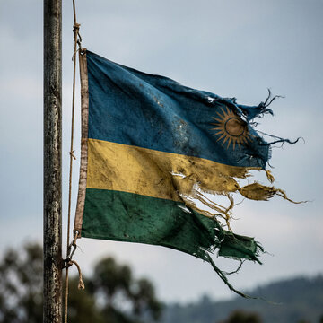 Heavily damaged and torn flag of rwanda flying on a pole under an overcast sky with rwandan flag east africa weathered distressed national patriotism political conflict independence identity