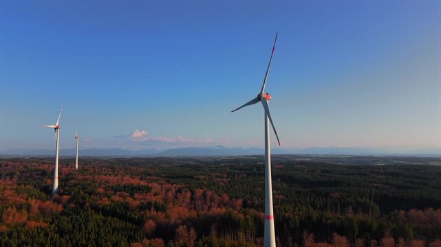 Aerial view of three wind turbines over autumn forest near Starnberg, Germany with Alps in background. Scenic landscape showing renewable energy, sustainability and modern wind power generation.
