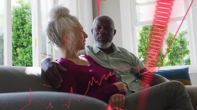 Couple sitting on sofa woman speaking causing overlaying red finance charts sweeping right on cash