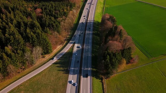 Drone shot of the Bundesautobahn 95 in Southern Germany. Modern road infrastructure and traffic flowing through the scenic Bavarian landscape towards the Alps on a sunny summer day.