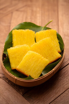 Potongan singkong kuning kukus tersaji di atas daun hijau dalam wadah bambu, tampak lembut, berserat, dan menggugah selera dengan warna cerah alami.