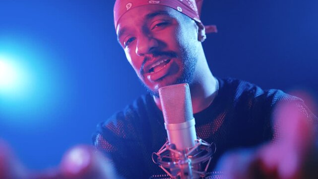 Charismatic latino singer performing a song in a professional microphone. Man rapping and gesturing with his hands in a studio with blue lights