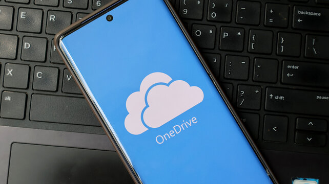 A smartphone displaying the OneDrive logo lies on a black laptop keyboard.