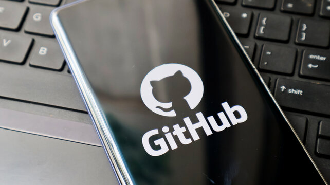 A smartphone displaying the GitHub logo lies on a laptop keyboard in a modern workspace