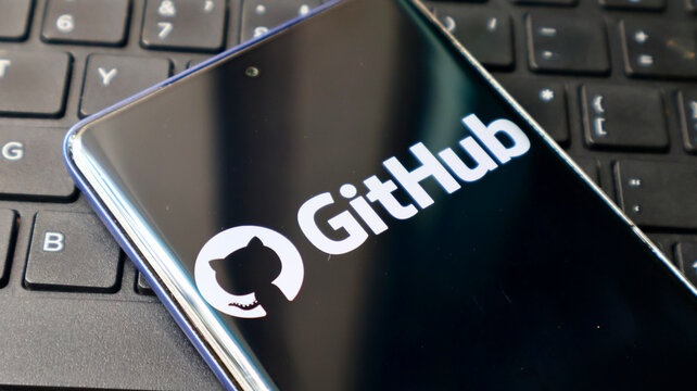 A smartphone displaying the GitHub logo on its screen rests on a computer keyboard