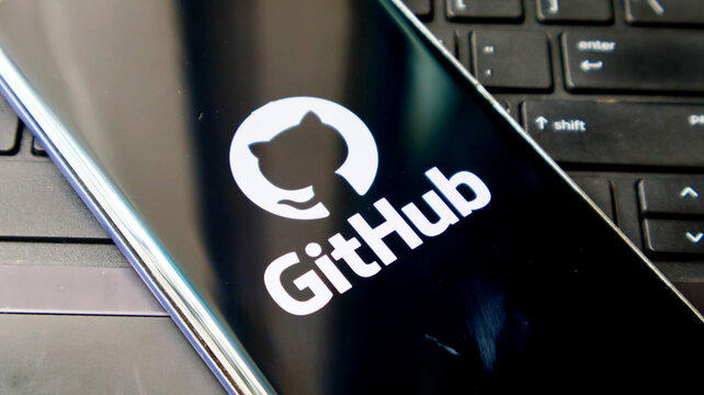 A smartphone displaying the GitHub logo on its screen next to a laptop keyboard